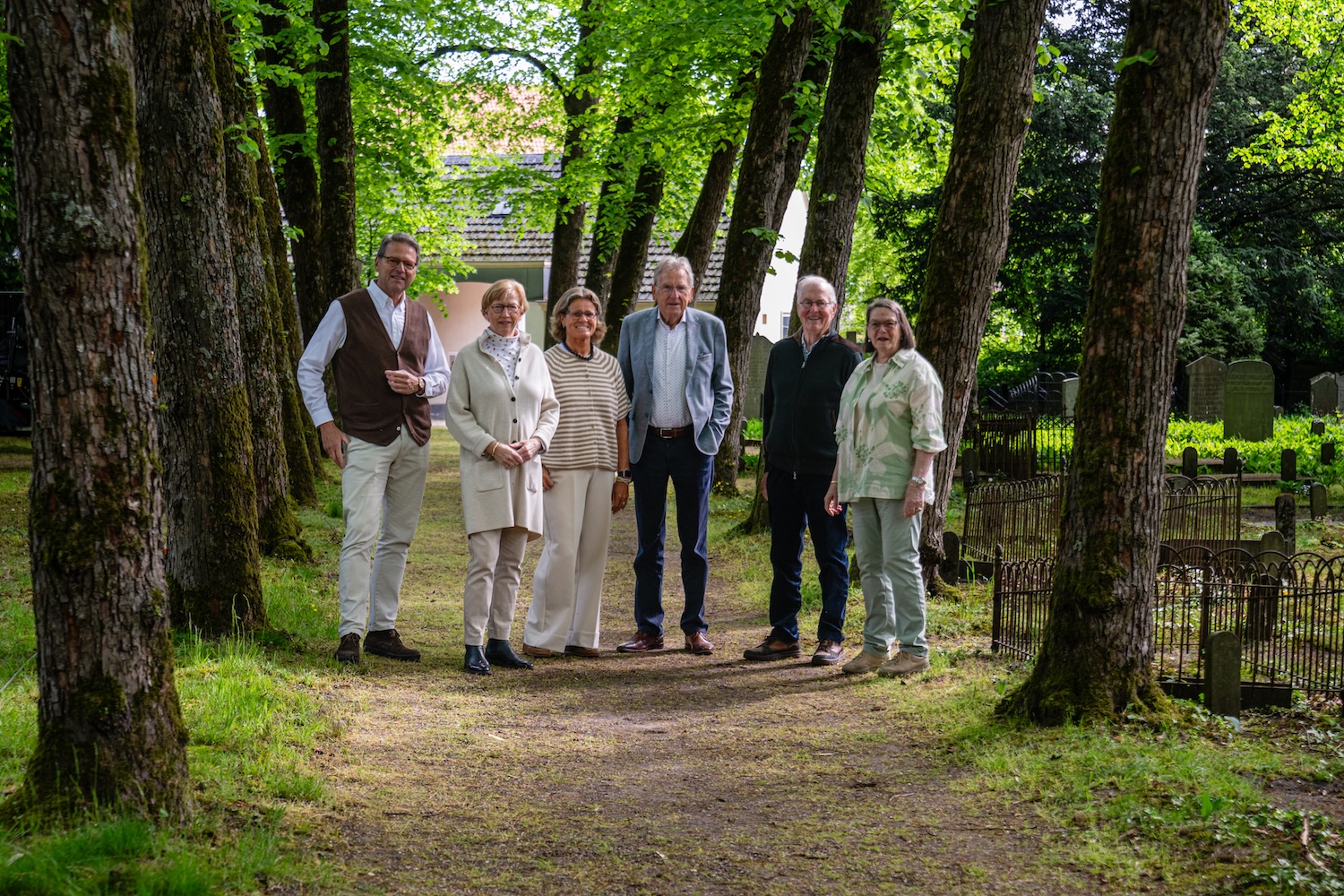 Bestuursleden van Stichting Oude Algemene Begraafplaats Zeist poseren bij het historische poortgebouw en tussen de graven op de begraafplaats in Zeist.